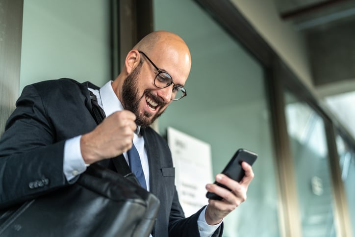 A business man pumps his fist as he looks at his mobile phone.