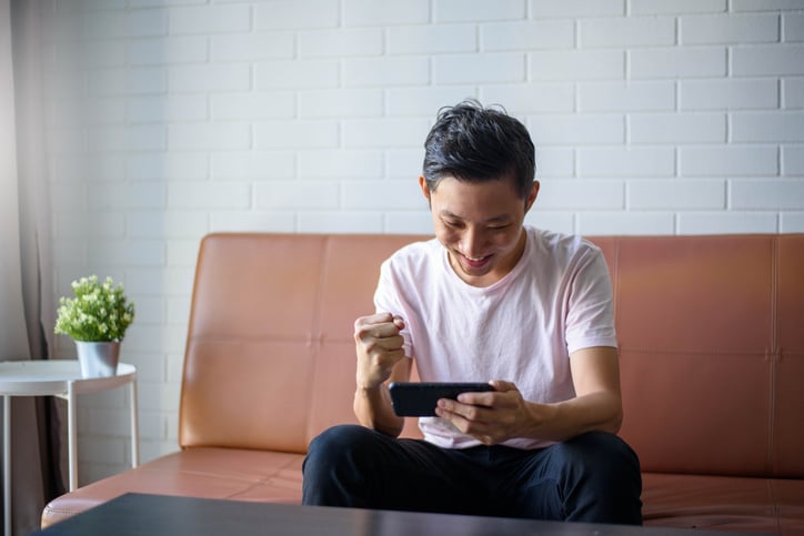 A man sits on a leather couch smiling as he looks at his mobile phone.